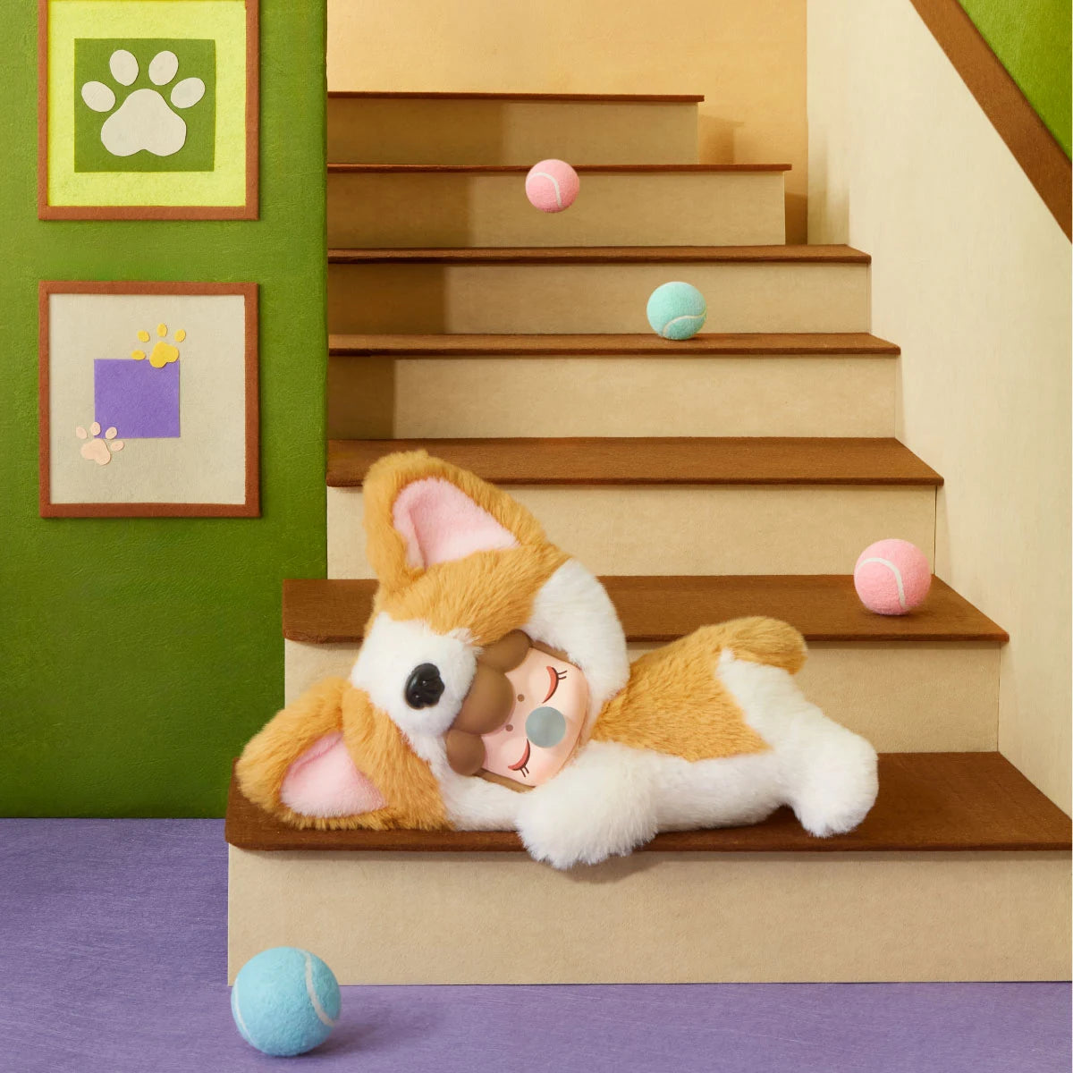 Orange-and-white Nanci Puppy Club Corgi plush doll lying across miniature wooden stairs, showing pointed ears and a sleeping face, surrounded by pastel balls and framed paw-print artwork.