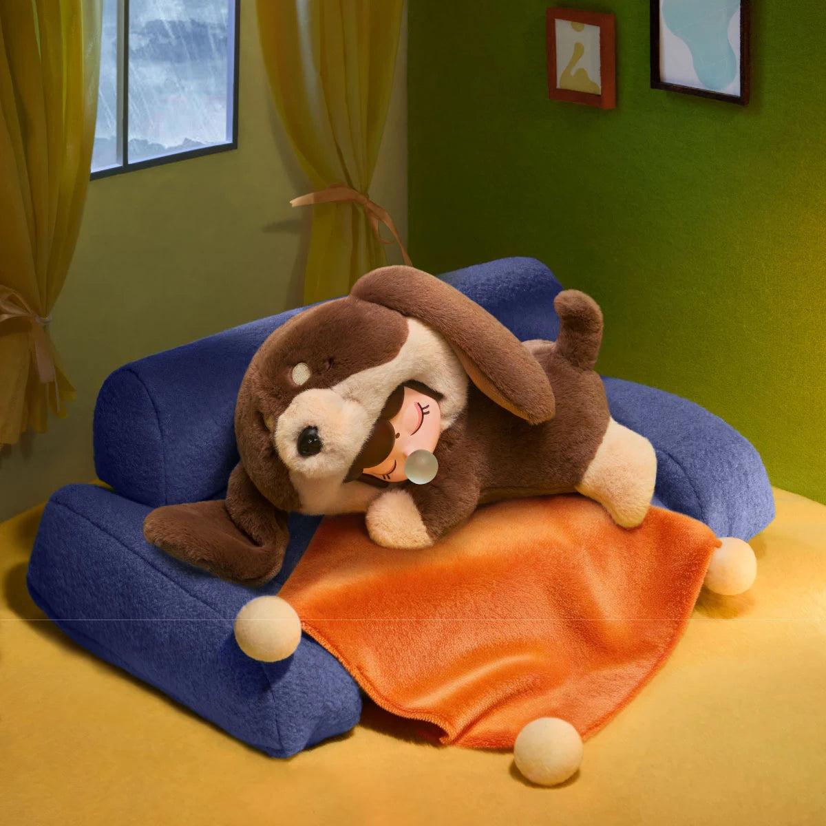 Brown-and-cream Nanci Puppy Club Dachshund plush doll resting on a blue miniature sofa with an orange blanket, beside a rainy window in a green-walled room.