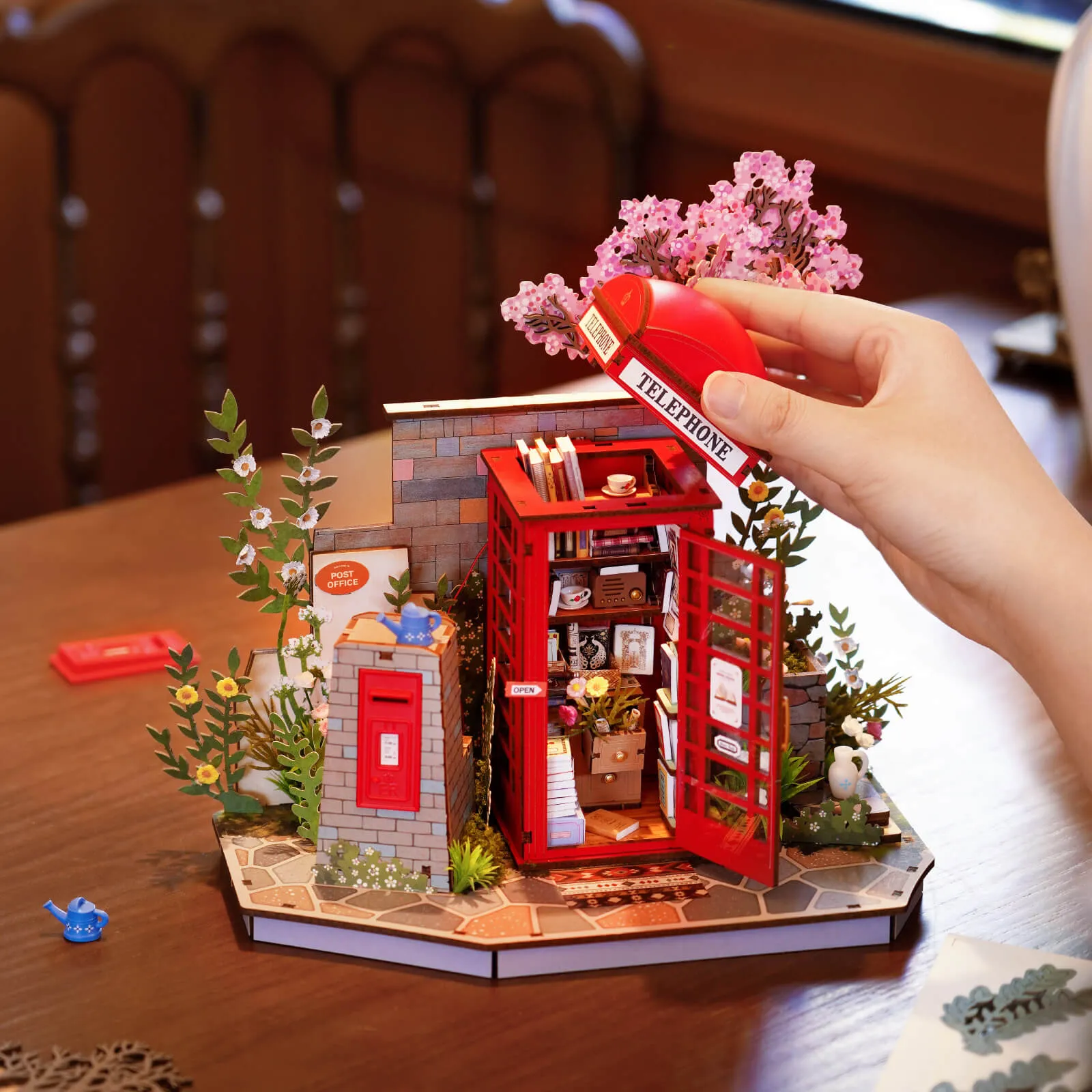 Mains plaçant des livres à l'intérieur du modèle de cabine téléphonique rouge Blossom Book Booth