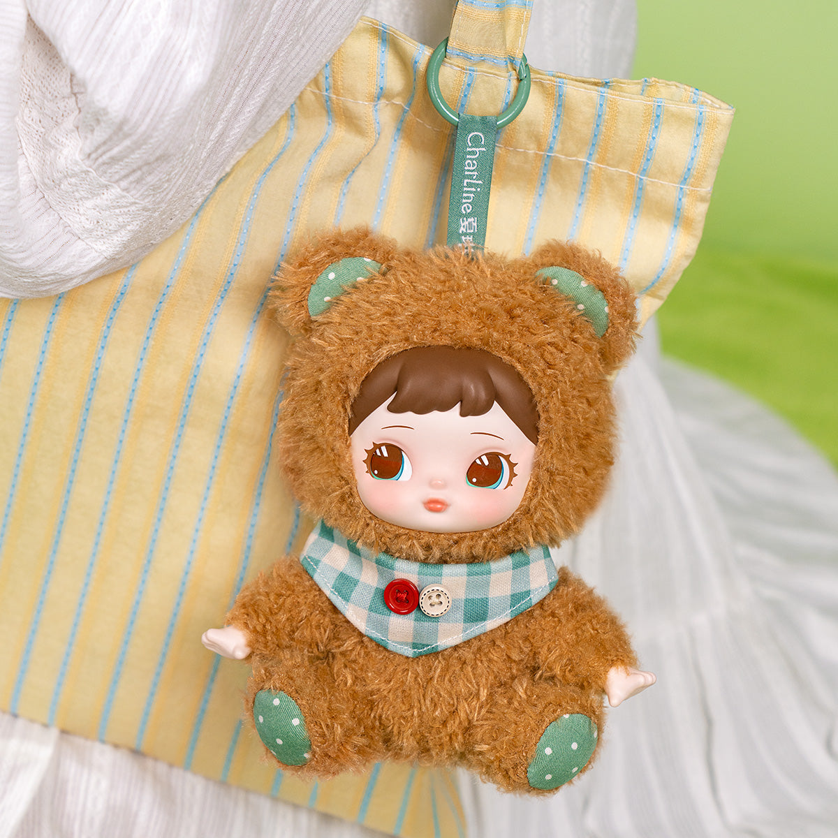 Charline Forest Hide and Seek Coco Bear plush pendant hanging on striped fabric