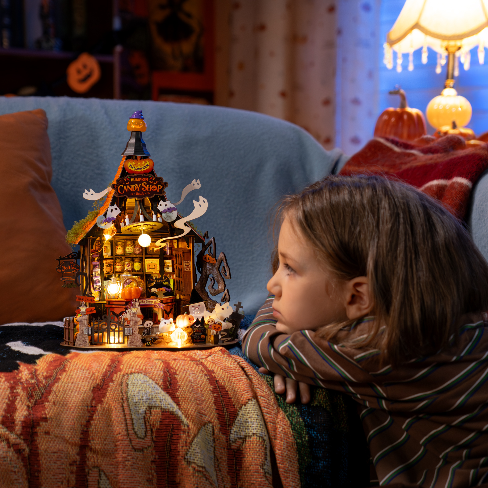 Child watching the glowing Rolife Haunted Candy House miniature in a cozy Halloween room