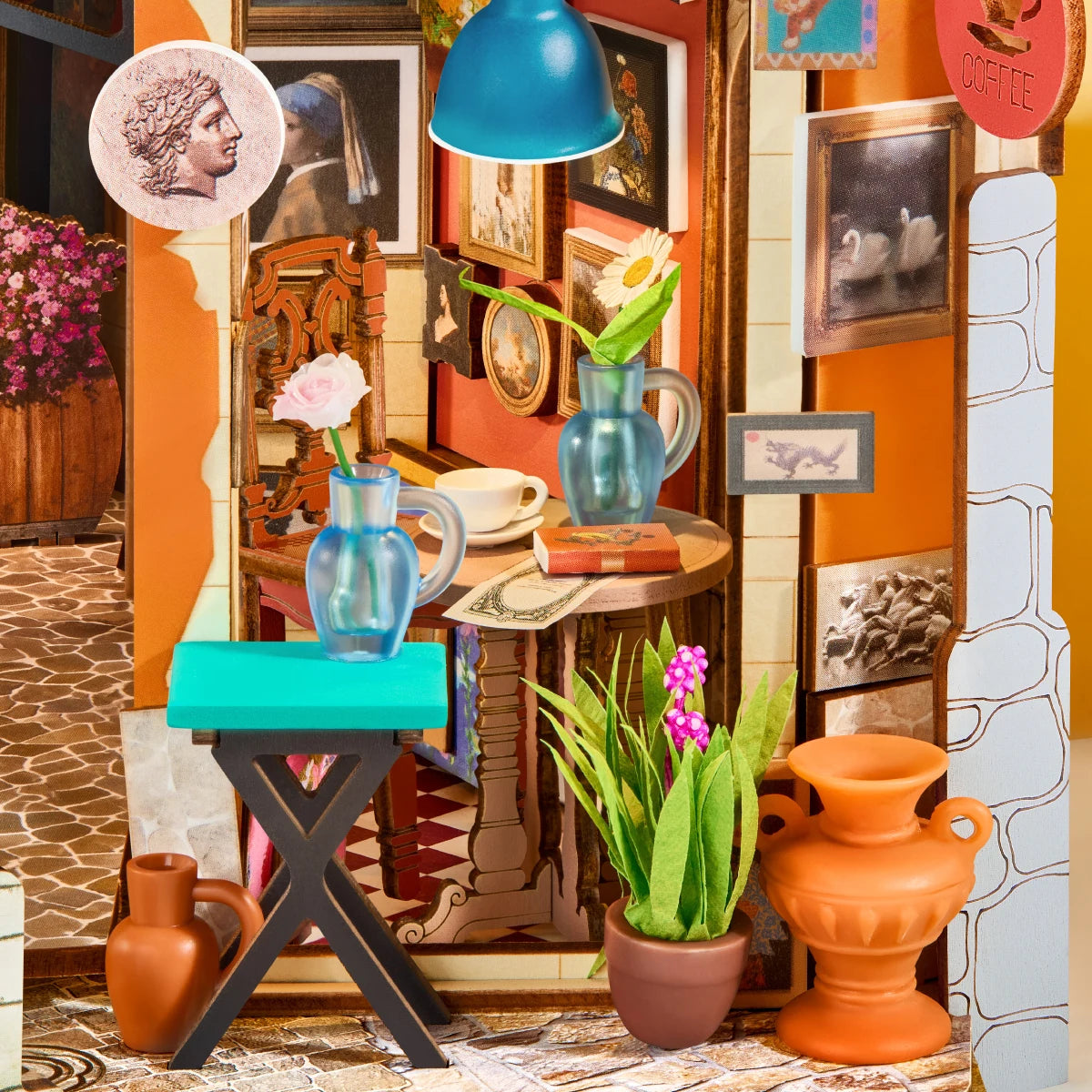 Close-up of the miniature art shop interior with framed paintings, blue pendant lamp, turquoise stool, vases, flowers, coffee cup and terracotta pots.