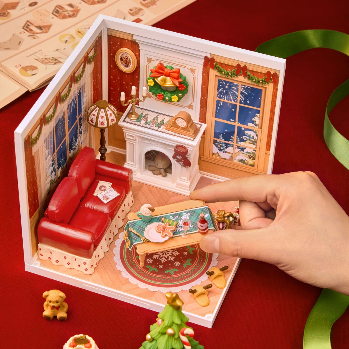 Hand placing a miniature bottle on the table inside a Rolife Christmas living room diorama, with instruction sheet and loose parts nearby.